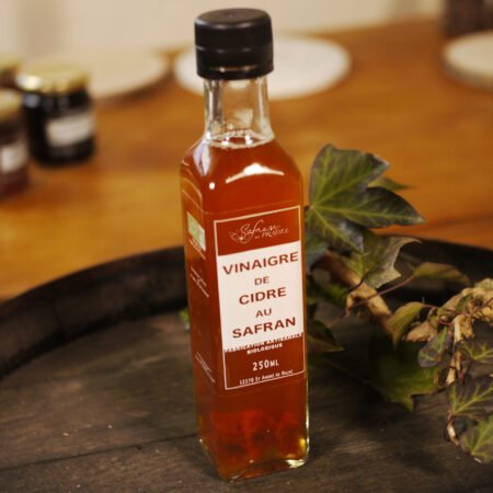 Présentation d'une bouteille de vinaigre de cidre au safran, sur le dessus d'un tonneau où un branche de lierre termine le décor. Logo de Safran du Pradel. En dessous, Fabrication artisanale biologique. 250ml