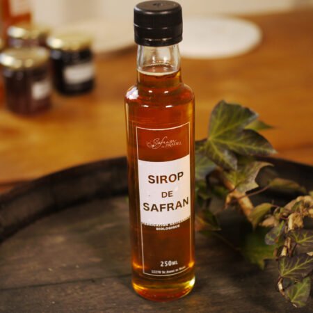La bouteille de sirop de safran de 250ml prend place sur un tonneau de bois décoré de lierre.